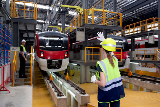 Young caucasian engineer woman or worker signal while engineer man checking electric train for planning maintenance in station, transport and infrastructure, inspector check service transport.