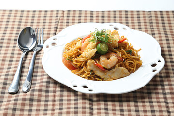 stir fried Malay spicy chilli noodle mamak mee goreng with mixed seafood fish, prawn, squid, meat and lime in plate on white background asian chef cuisine halal food menu for cafe