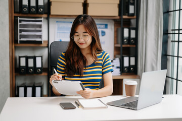 Confident Asian woman with a smile standing holding notepad and tablet at the modern office.