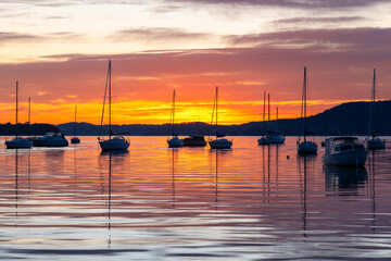 Sunrise over the water with boats, reflections and high cloud