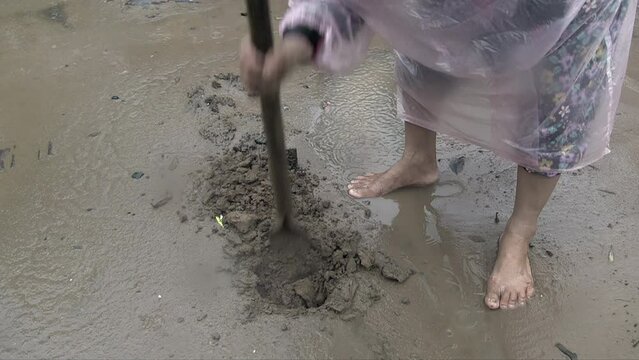 close up of a woman wearing a raincoat digs a hole in the ground with a spade round under the rain