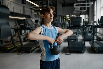 Closeup young sportive boy training with weights lifting kettlebell