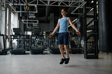 Fototapeta na wymiar Sportive teenage boy skipping rope while training at gym