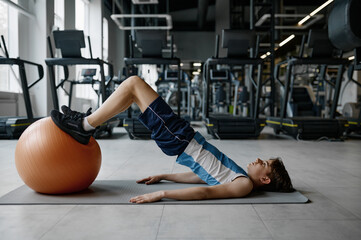 Teenager boy lying on mat doing physical exercise with fitness ball