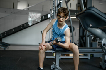 Fototapeta na wymiar Skinny nerd boy doing lifting workout with dumbbells training at gym