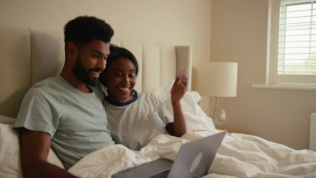 Couple at home in bed making video call on laptop computer - shot in slow motion
