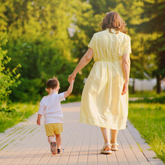 The woman walks down the path with her baby. Child holds onto his mother's hand tightly, feeling...