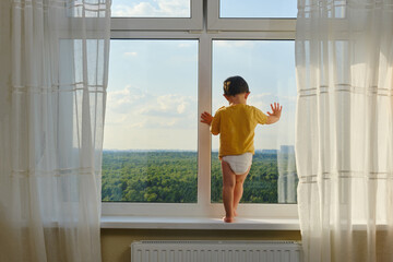 The child is precariously perched on the window sill, looking out the window and risking a fall....