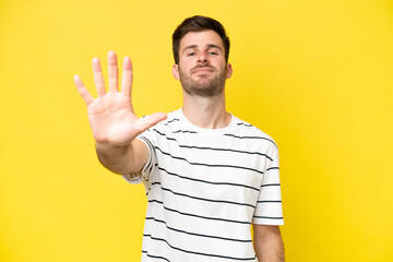 Young caucasian man isolated on yellow background counting five with fingers