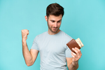 Young caucasian man holding a wallet isolated on blue background celebrating a victory