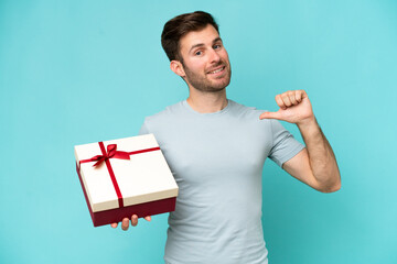 Young caucasian man holding a gift isolated on blue background proud and self-satisfied