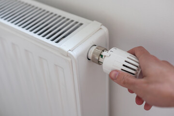 Hand adjusting thermostat valve of heating radiator in a room.