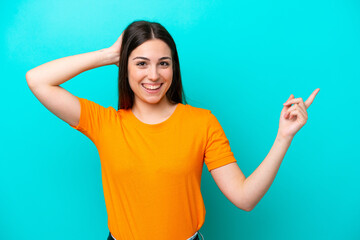 Young caucasian woman isolated on blue background surprised and pointing finger to the side