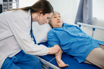 Obraz premium Doctor in white suit take notes while discussing and Asian elderly, woman patient who lying on bed with receiving saline solution in hospital or clinic.