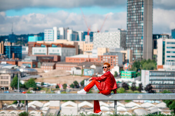 Fototapeta na wymiar a red hair woman in a red costume sitting in front of the city on great summer day