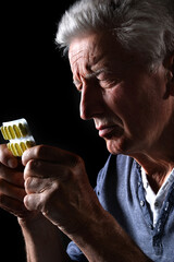 Close-up portrait of sad sick senior man holding pills