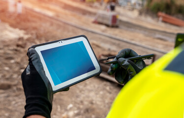 Site engineer surveyor using rugged tablet controller computer to operate EDM total station for...