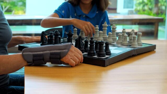 The hands of the grandmother and grandson of chess players on the table in the house. Board games.