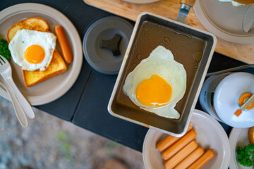 Breakfast on the table. Asian couple cooking food fried egg and bread with sausage at camp. Man and woman enjoy outdoor lifestyle travel nature and camping together on summer holiday vacation.
