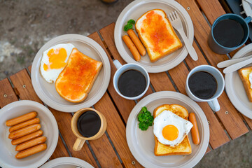 Breakfast on the table. Asian couple cooking food fried egg and bread with sausage at camp. Man and woman enjoy outdoor lifestyle travel nature and camping together on summer holiday vacation.