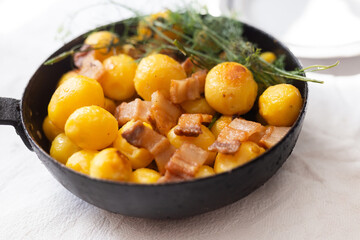 Fried new potatoes with bacon and dill in a frying pan