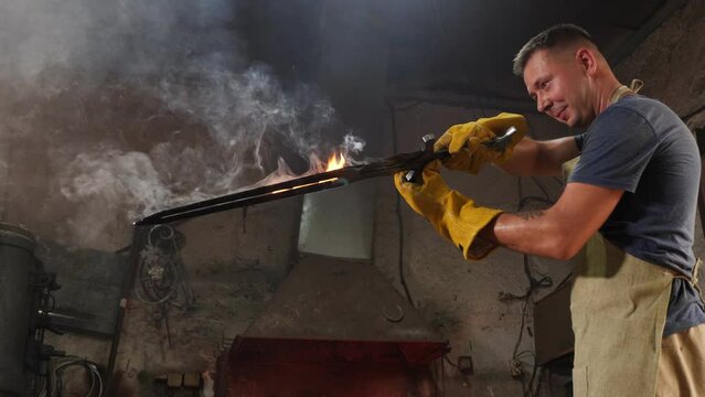 A strong blacksmith forged a large sword in an ancient forge, he holds a red-hot sword with sparks and smoke.