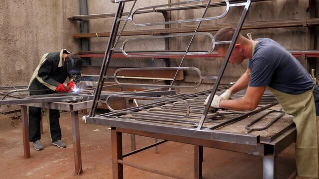 Two blacksmiths make metal railings for stairs, they grind and weld metal. Worker grinding in a workshop. Heavy industry factory, metalwork. 