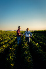 Two farmers in soy field making agreement with handshake at sunset.