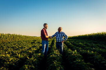 Two farmers in soy field making agreement with handshake at sunset.