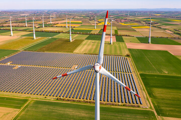 Aerial of a wind turbine from drone view in front of fields and solar panels