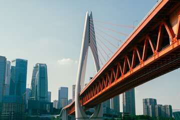 Low angle view of suspension bridge against sky with skycrapers and a river in the background