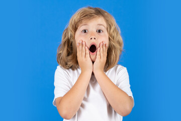 Shocked child boy keeping hands near cheek with open mouth on studio isolated background. Surprised...