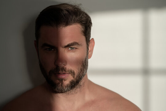 Closeup Beauty Portrait Of Satisfied Young Man After Facial Cream. Attractive Brunet Guy Touching Skin. Men Model Face With Beard And Modern Haircut. Male Coscmetic And Beauty Concept.