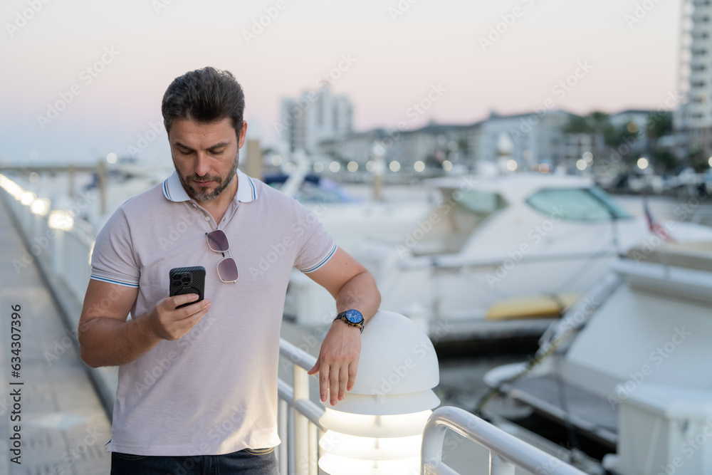 Wall mural Portrait of handsome man chatting on phone in city. Confident man talking on phone in modern big american city. Stylish lambersexual model. Sexy man dressed in polo. Bisiness phone conversation.