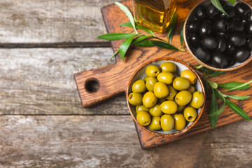 Green and black olives, olive oil on a brown wooden background. Fresh juicy olives in a bowl and fresh olive leaves. Vegan. Olive fruits. Place for text. Copy space.