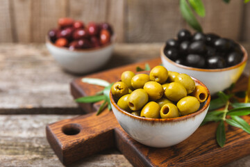 Green, black and red olives, olive oil on a brown wooden background. Fresh juicy olives in a bowl and fresh olive leaves. Vegan. Olive fruits. Place for text. Copy space.