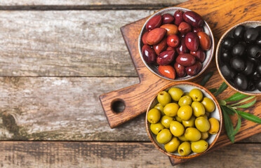 Green, black and red olives, olive oil on a brown wooden background. Fresh juicy olives in a bowl and fresh olive leaves. Vegan. Olive fruits. Place for text. Copy space.