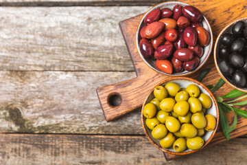 Green, black and red olives, olive oil on a brown wooden background. Fresh juicy olives in a bowl and fresh olive leaves. Vegan. Olive fruits. Place for text. Copy space.