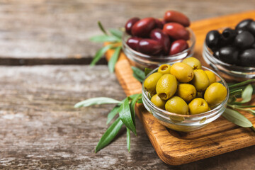 Green, black and red olives, olive oil on a brown wooden background. Fresh juicy olives in a bowl and fresh olive leaves. Vegan. Olive fruits. Place for text. Copy space.