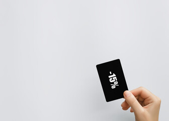 a woman's hand holds a minus 15 percent discount card on a gray background. sales, marketing,...