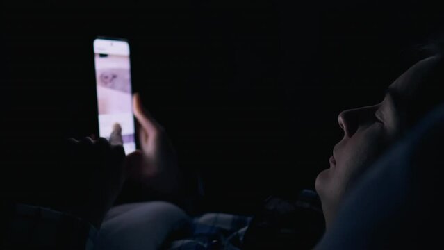 Phone addiction young woman looks at the bright screen of the smartphone at night, Addiction to social networks, The bright screen of the smartphone in the hands of a girl who lies in bed at night