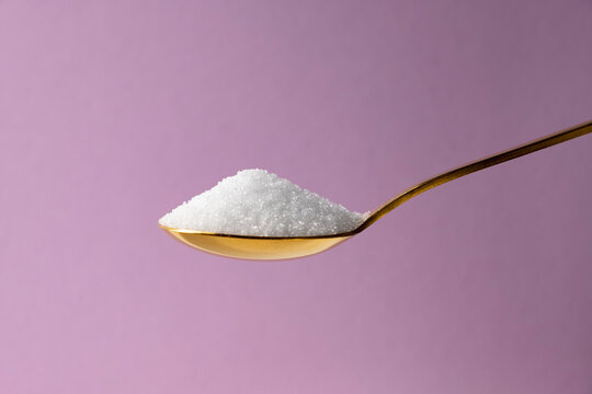 Erythritol in a golden spoon on a lilac background. Diet, healthy food concept.
