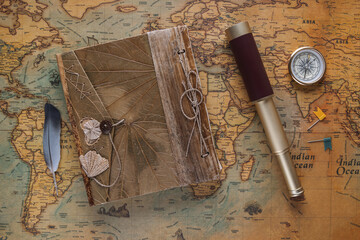 Spyglass, a compass, a vintage leather book and a bird's feather - a symbol of travelers lie on an old map. View from above