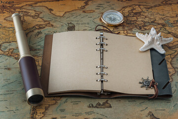 Open leather book with blank pages for writing text or a logo, a spyglass, a starfish and a brass compass lie on a vintage map