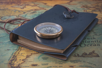 Brass compass and a leather-bound book lie on an old map. Close-up