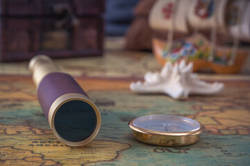 Spyglass, a brass compass and a starfish lie on an old map against the background of a wooden model of a sailboat. Close-up