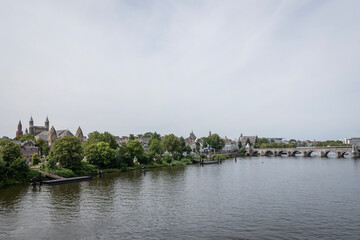 Fototapeta na wymiar Rooftop of The Basilica of Our Lady religious Roman Catholic building landmark in Maastricht city Netherlands. Trees line the banks of the river Meuse with small wooden dock