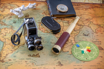 Vintage film camera with cassettes, spyglass, leather bound book and brass compass on an old nautical chart