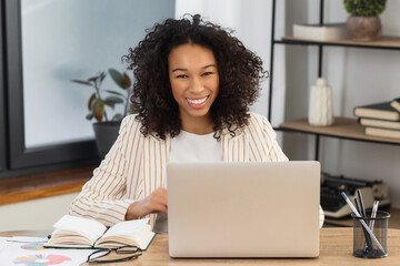 Fototapeta na wymiar Young successful African American woman entrepreneur or CEO sitting in the workplace in a modern office looking at camera and smiling friendly