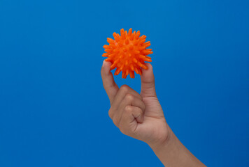 Child holding spiky orange massage needle ball by fingers over blue background © Tatiana Foxy